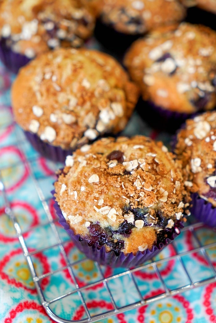 Blueberry muffins with oat crumble topping on a wire cooling rack, colorful patterned cloth underneath&mdash;an easy muffin recipe perfect for any occasion.