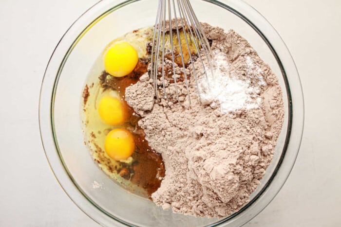 A mixing bowl filled with eggs, flour, cocoa, and baking powder is being whisked together to create a rich brownie mix.