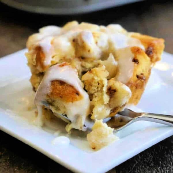 A fork cutting into a gooey cinnamon roll muffin topped with icing on a white plate, reminiscent of homemade monkey bread muffins.