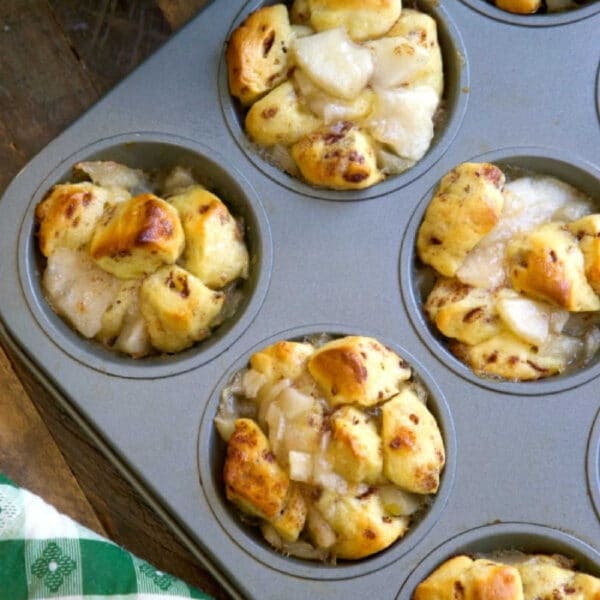 Muffin tin with baked apple pie monkey bread muffins, some golden brown and filled with diced apples.