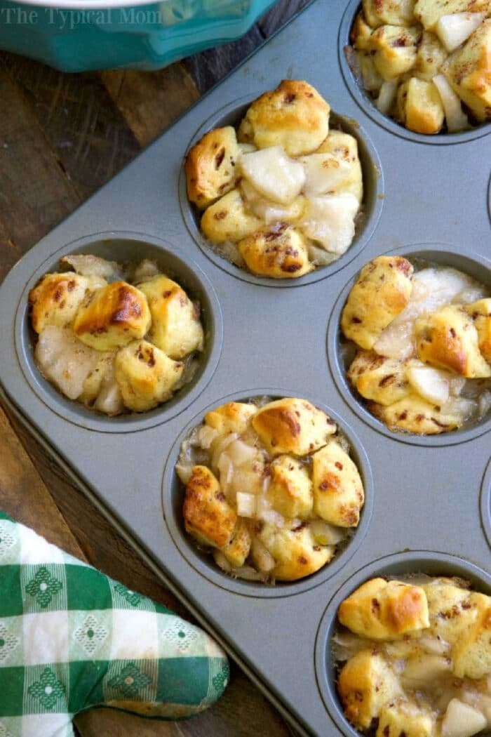 Muffin tin with baked apple pie monkey bread muffins, some golden brown and filled with diced apples.
