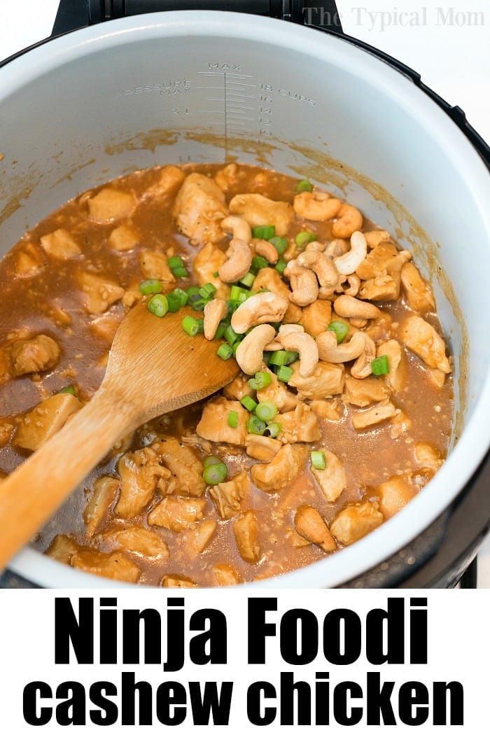 Pressure cooker cashew chicken with sauce, green onions, and cashews in a Ninja Foodi pot, stirred with a wooden spoon.