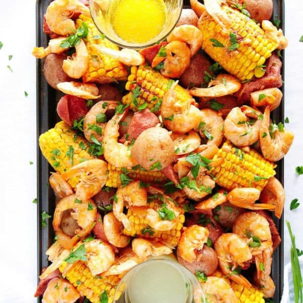 Tray filled with instant pot shrimp boil goodness—shrimp, corn, potatoes, and sausage—served with two dipping sauces on the side.