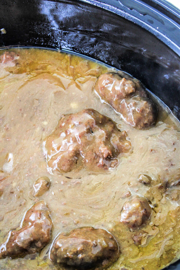 Beef tips covered in brown gravy simmer in a black slow cooker, creating a comforting Chopped Steak Recipe that's perfect for any meal.