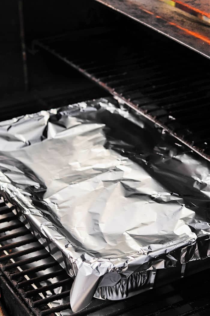 A foil-covered baking pan with smoked chuck roast sits on the rack inside a grill or oven.