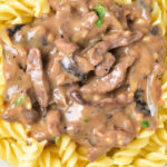 A plate of rotini pasta topped with rich venison stroganoff, garnished with fresh parsley.