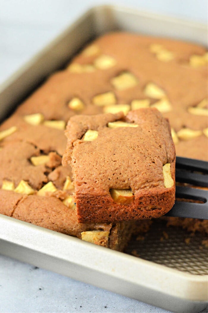 A slice of apple cake with cake mix is being lifted from a baking pan with a spatula.