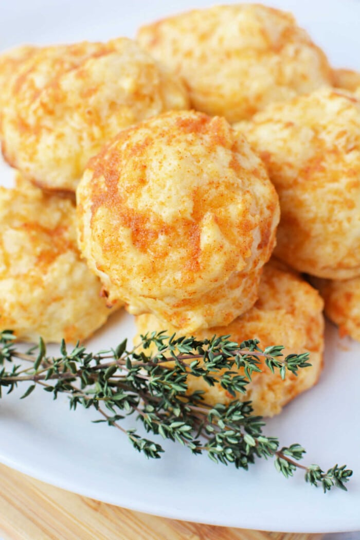 Jiffy Mix cheddar biscuits stacked on a white plate with a sprig of thyme garnish.