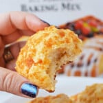 A hand holding a bitten cornbread muffin in front of a Jiffy baking mix box, showcasing the perfect start to any biscuits recipe.