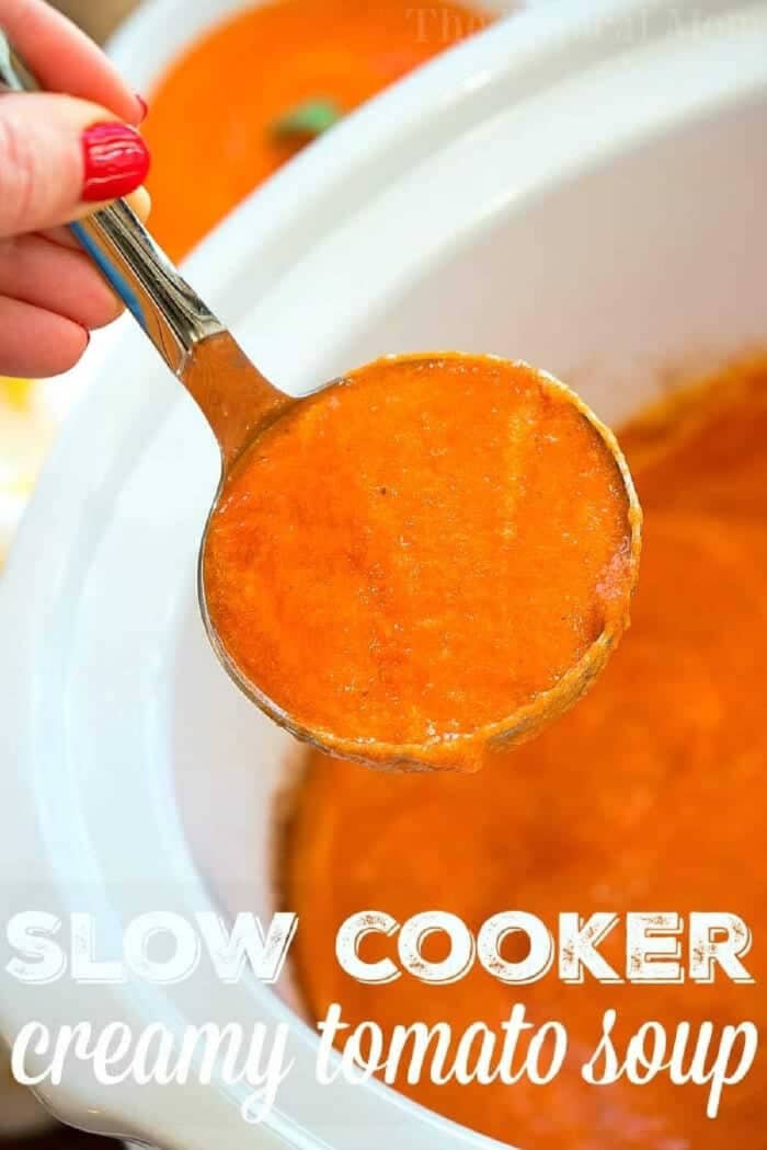 A hand holds a ladle of Creamy Tomato Soup above a slow cooker brimming with the comforting soup.