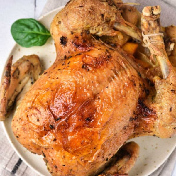 Instant Pot whole chicken with crispy golden skin served on a white plate, garnished with fresh spinach leaves.