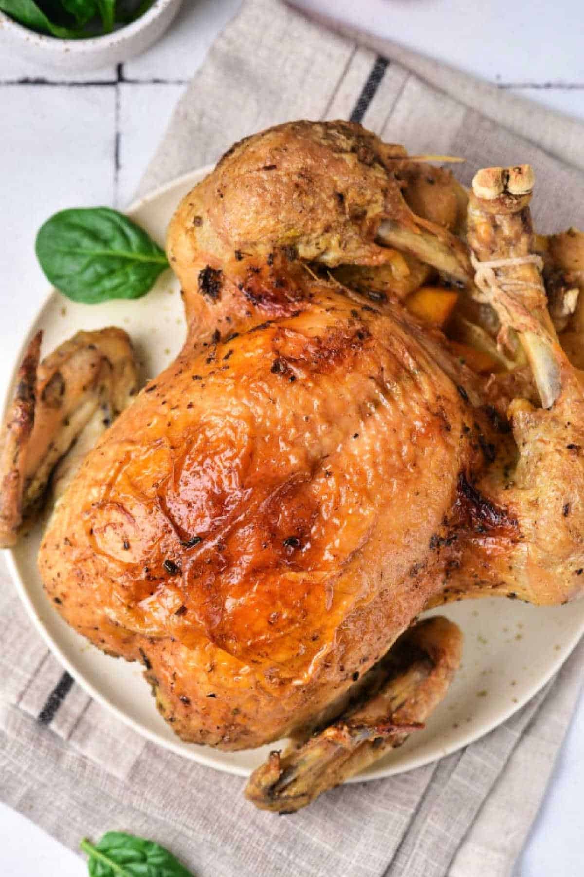 Instant Pot whole chicken with crispy golden skin served on a white plate, garnished with fresh spinach leaves.