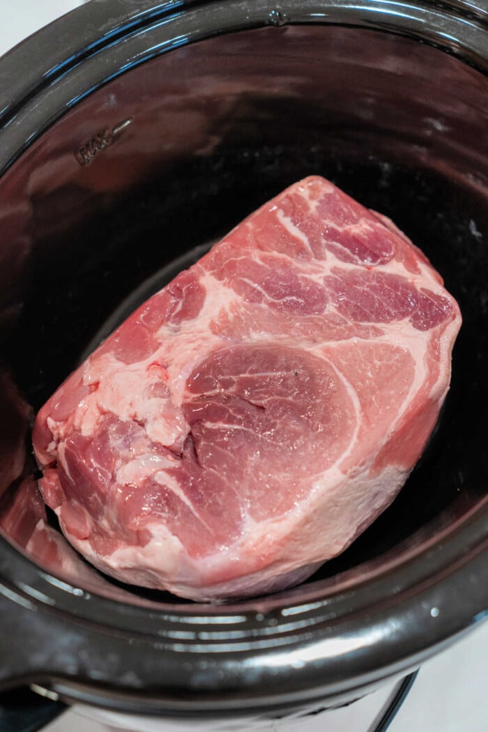 A large raw pork roast set inside a slow cooker is the perfect start to an easy pulled pork recipe.