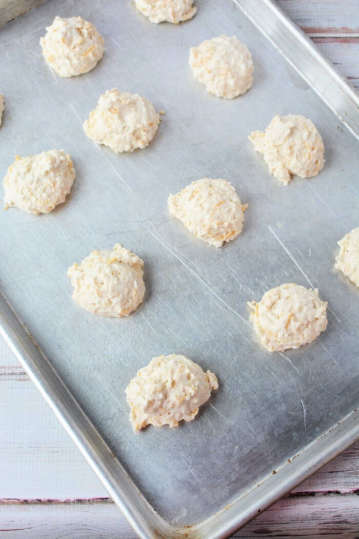 Dollops of Jiffy Mix biscuit dough spaced on a metal baking sheet.