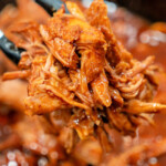 Close-up of tender pulled pork on tongs, drenched in sauce, captioned 2 Ingredient Pulled Pork Recipe.