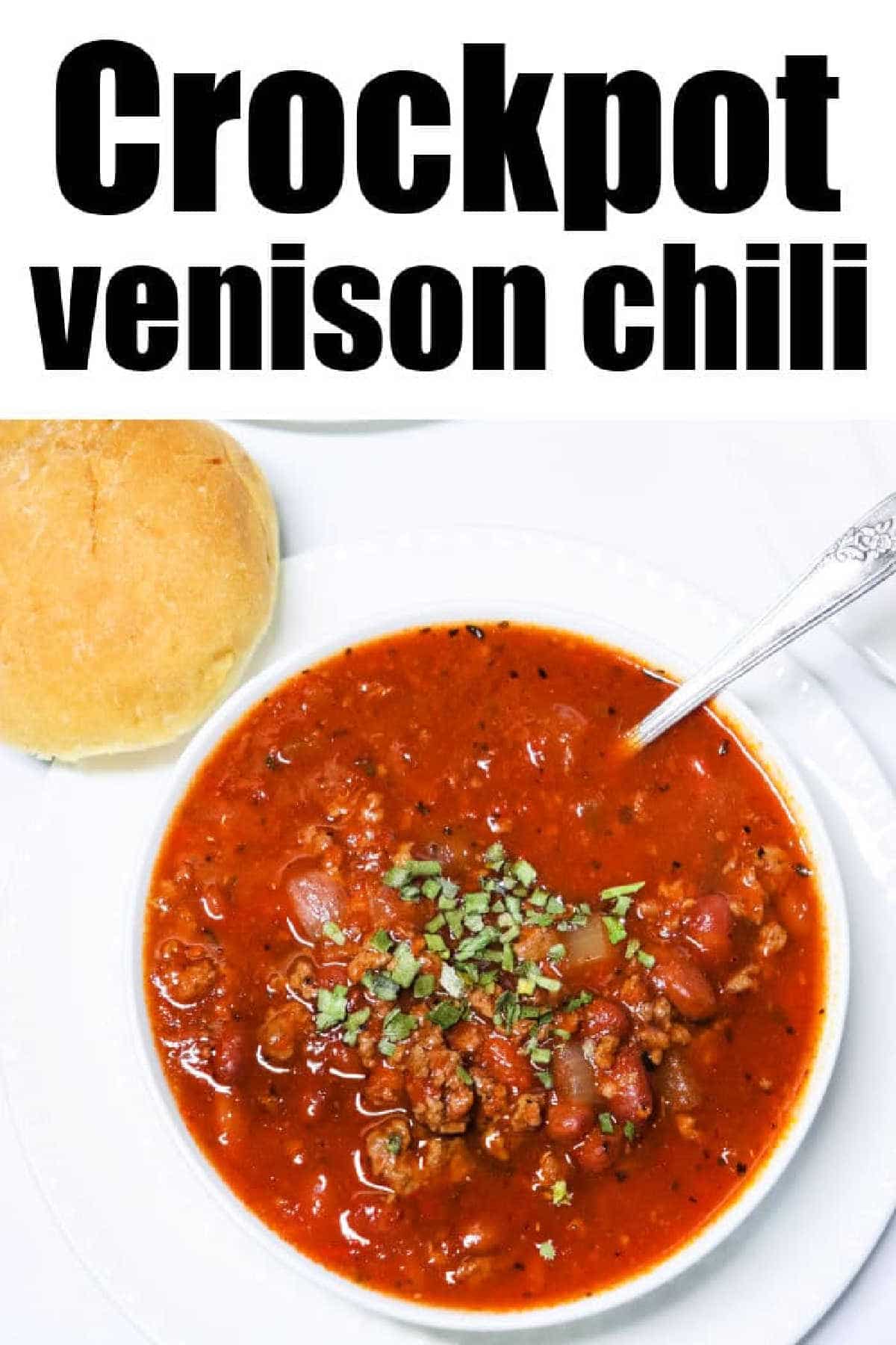 A hearty bowl of Venison Chili topped with fresh herbs, served alongside a warm bread roll.