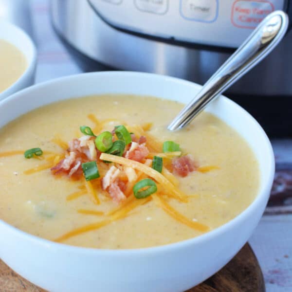 A bowl of creamy potato soup topped with cheese, crispy bacon, and green onions sits invitingly with a spoon beside it, fresh from the pressure cooker.