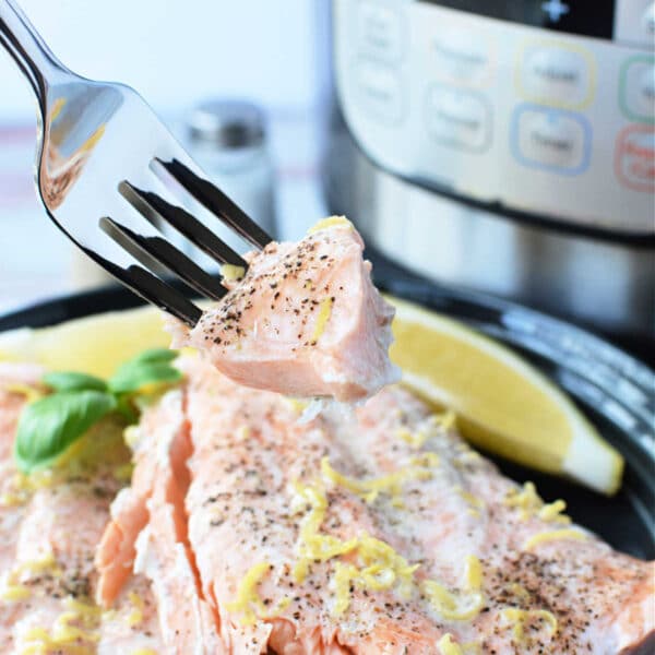 A fork holds a tender piece of salmon, perfectly cooked and garnished with lemon zest and pepper. Nearby, lemon wedges accompany the dish, hinting at the flawless results achieved with a pressure cooker.