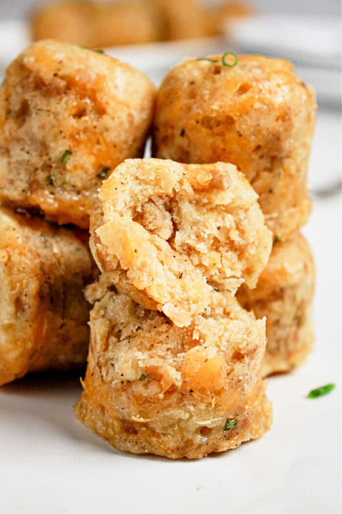 Close-up of stacked, golden-brown savory muffins with a cracked one on top, revealing a soft, textured interior—an inviting sight reminiscent of warm sausage balls fresh from the pressure cooker.