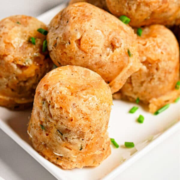 Round sausage balls made in a pressure cooker, are garnished with chopped chives on a white square plate.