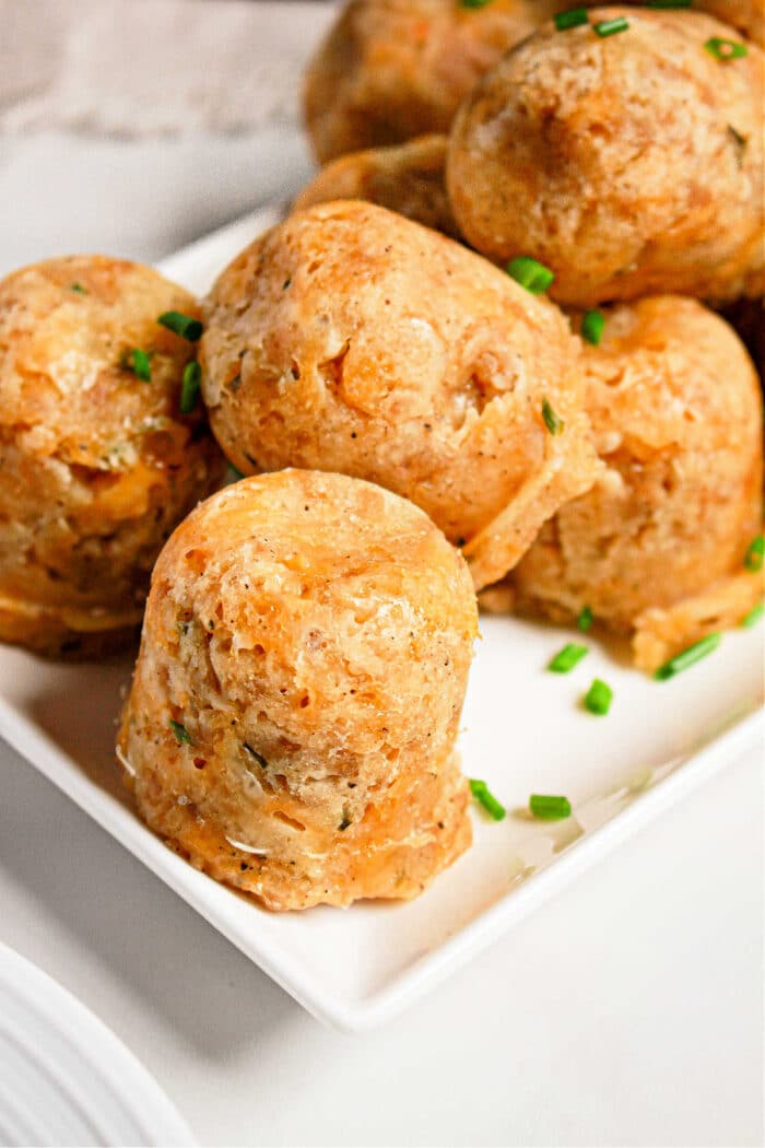 Round sausage balls made in a pressure cooker, are garnished with chopped chives on a white square plate.