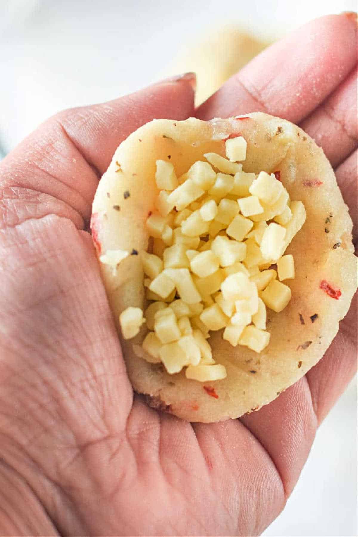 A hand holds mashed potatoes filled with small cubes of cheese, ready to be baked—perfect as a side for Air Fryer Mashed Potato Balls.