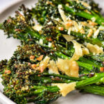 Air Fryer Broccolini roasted to perfection, topped with shaved parmesan cheese and minced garlic, served on a light-colored plate.