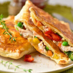 Golden flaky chicken pot pie puff pastry filled with tender chicken, peas, corn, carrots, and red peppers on a white plate.