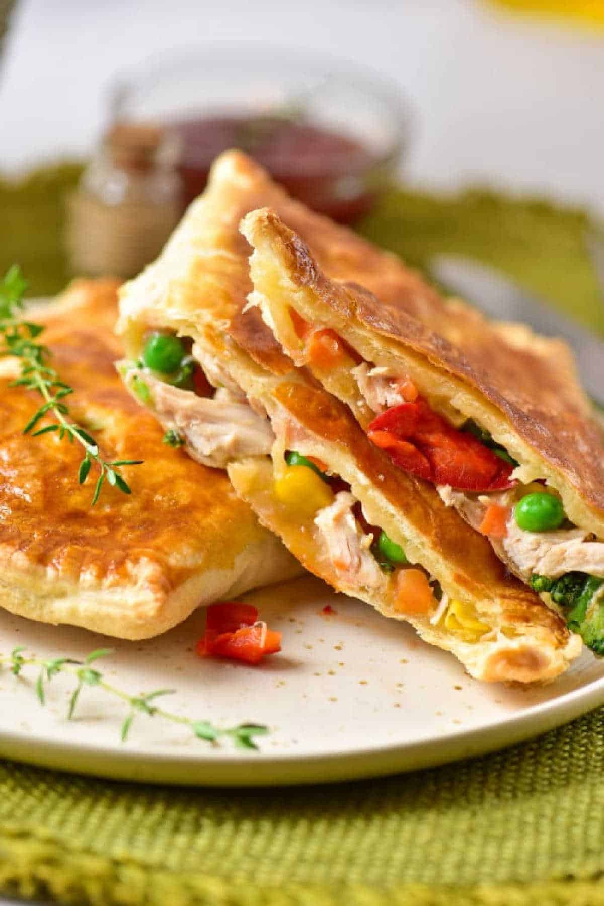 Golden flaky chicken pot pie puff pastry filled with tender chicken, peas, corn, carrots, and red peppers on a white plate.
