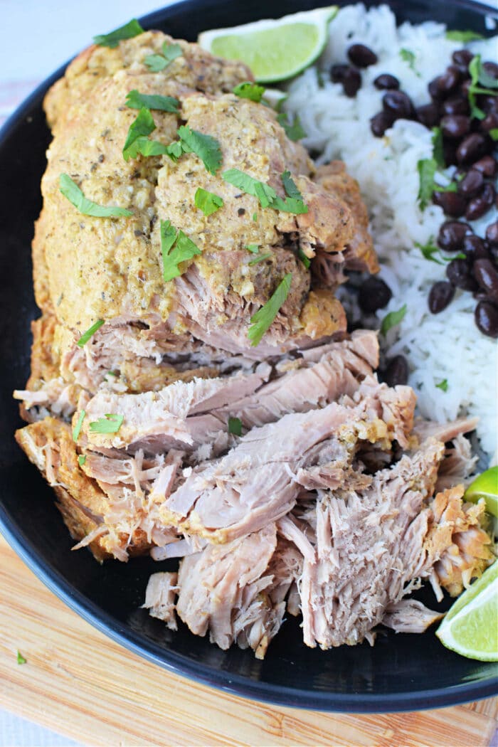 Savor shredded pork with herbs, paired perfectly with white rice and black beans, all garnished with lime wedges on a black plate—an exquisite roast recipe for any culinary enthusiast.