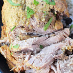 Close-up of shredded boneless pork sirloin roast garnished with herbs on a plate, complemented by rice and black beans on the side.