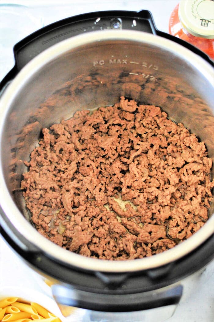 Instant Pot frozen ground beef browning perfectly, with dry pasta and a sauce jar ready on the counter for a quick and easy meal.