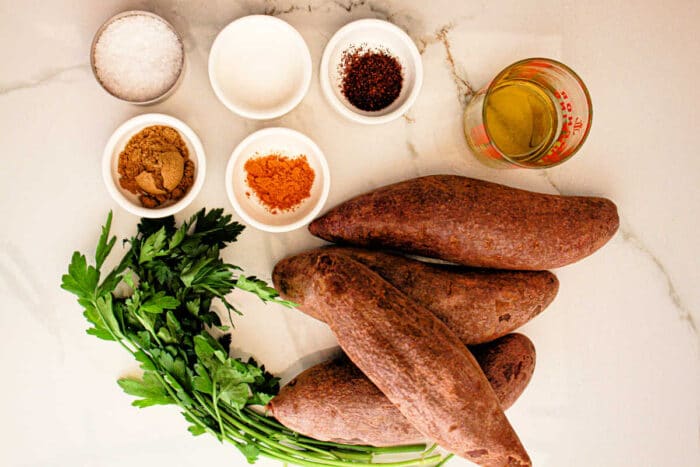 On a marble surface lay small bowls brimming with vibrant sweet potatoes, fresh parsley, and savory seasonings, setting the stage for a delightful recipe that could easily feature the rich hues of the purple sweet potato.