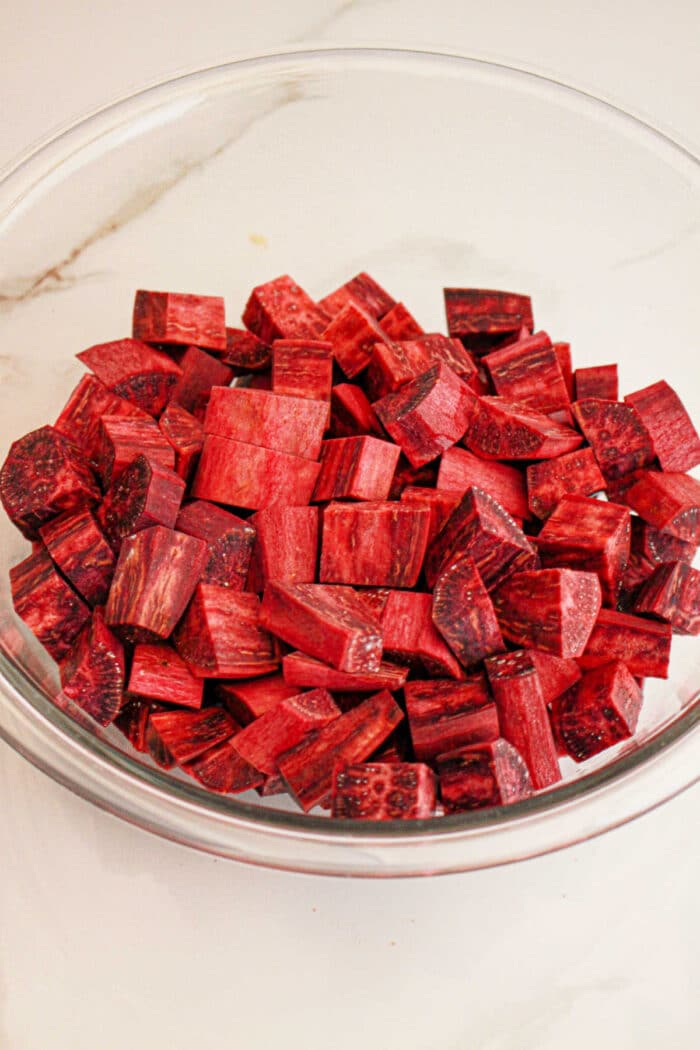 A glass bowl filled with cubed pieces of fresh purple yam, perfect for your next purple sweet potato recipe, rests on a white surface.