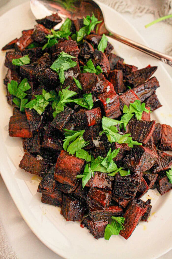 Cubed vibrant purple sweet potatoes sit elegantly on a white plate, complemented by a handy spoon.