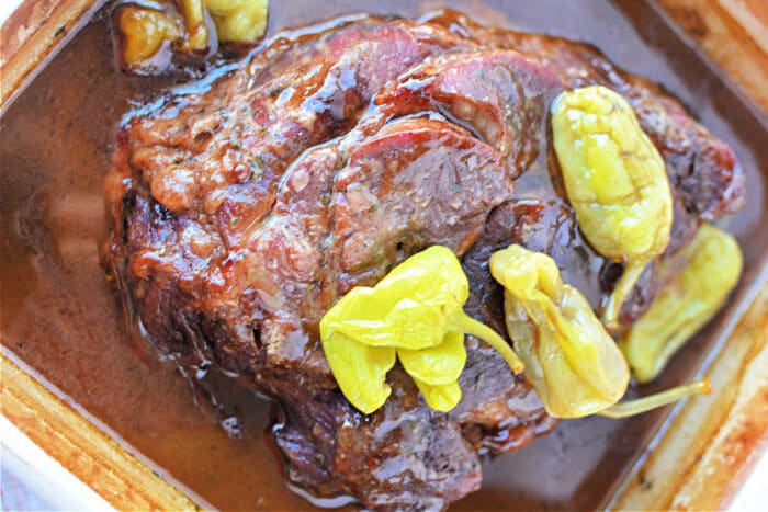 A cooked Mississippi Pot Roast Recipe in brown gravy topped with several whole yellow-green pepperoncini peppers.