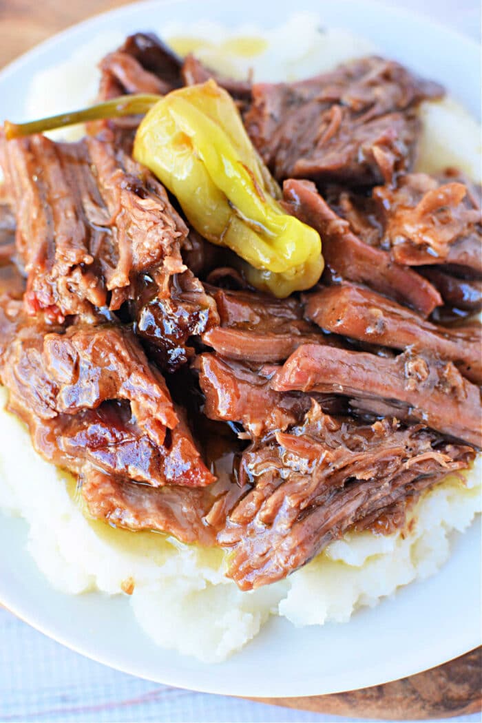 Shredded pot roast with gravy and a pepperoncini on mashed potatoes, served on a white plate&mdash;our Mississippi Pot Roast Recipe delivers classic comfort in every bite.