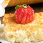 A slice of flaky bread topped with a sliced strawberry, reminiscent of the lightness found in a pineapple angel food cake recipe, served on a white plate.
