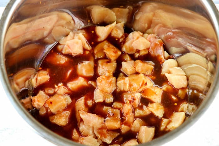 Diced raw asian chicken in a metal bowl, marinating in a dark sauce.