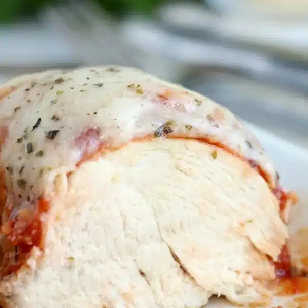 A close-up of instant pot chicken parmesan: sliced, baked chicken breast topped with melted cheese, tomato sauce, and herbs on a plate.