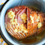 A spiral-cut ham with pineapple chunks and juice in a Ninja Foodi, ready to be cooked to perfection.