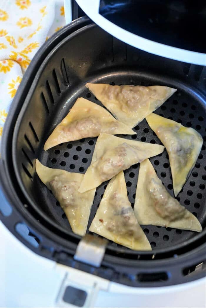 Seven uncooked air fryer won tons are arranged inside the basket, ready to be cooked to crispy perfection.