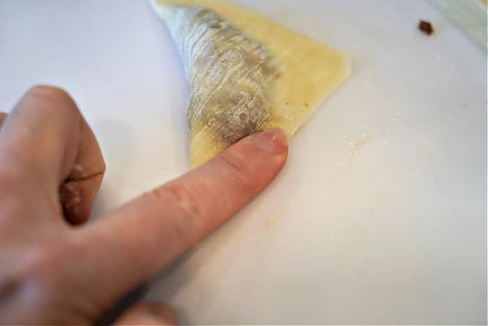 A hand folding dough over a savory filling on a white surface, preparing air fryer won tons for a crispy, golden snack.