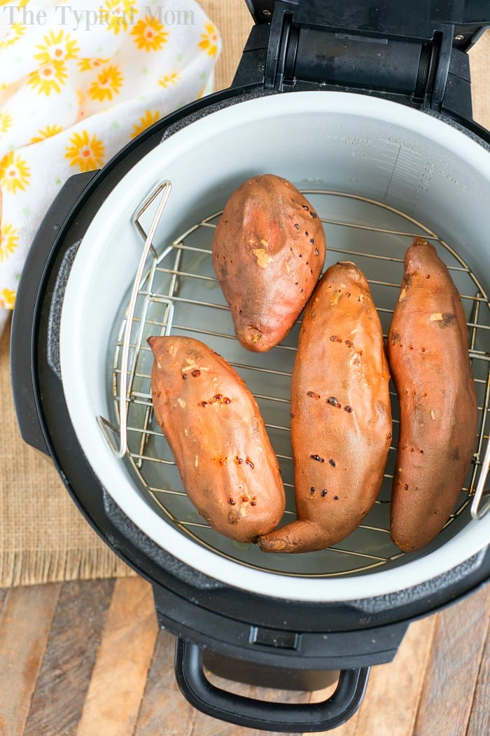 Four whole sweet potatoes on a metal rack inside an open electric pressure cooker, offering a similar tender result to making sweet potato in the air fryer.