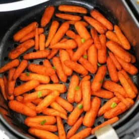 Air fryer carrots are seasoned baby carrots cooked to perfection in an air fryer basket, then garnished with a sprinkle of chopped green herbs.