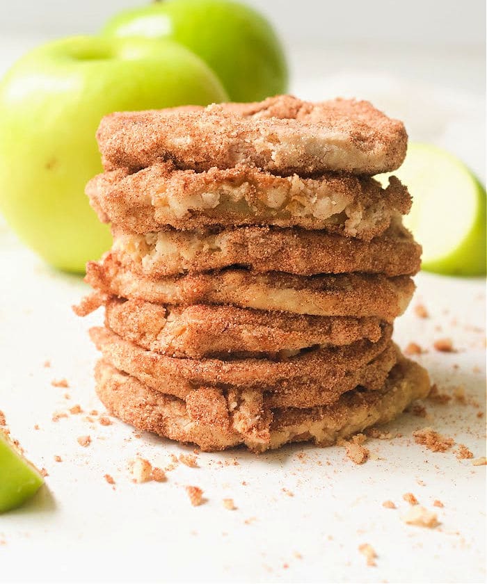 A stack of cinnamon sugar apple cookies with green apples and air fryer apples in the background.