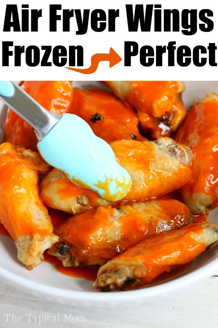 Tongs coating saucy buffalo wings in a white bowl with text: Frozen chicken wings in air fryer cooked to perfection.