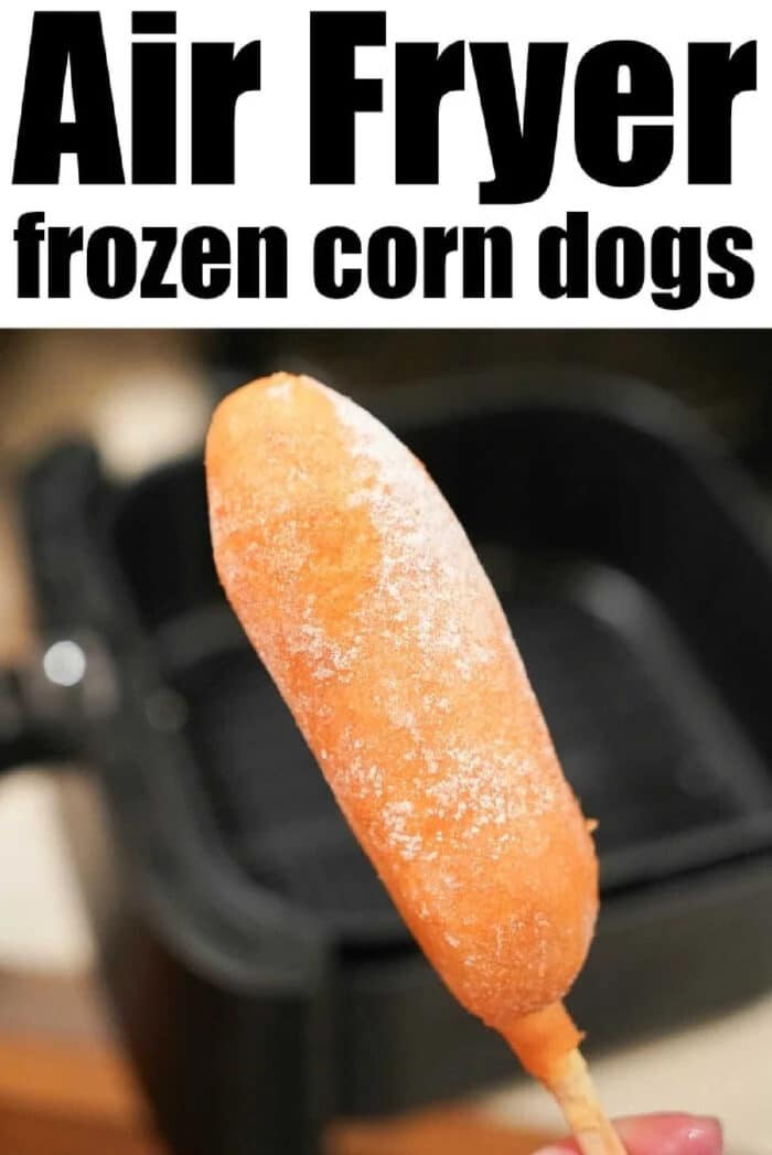 A hand holds a frozen air fryer corn dog in front of an open air fryer, ready for a quick and tasty snack.