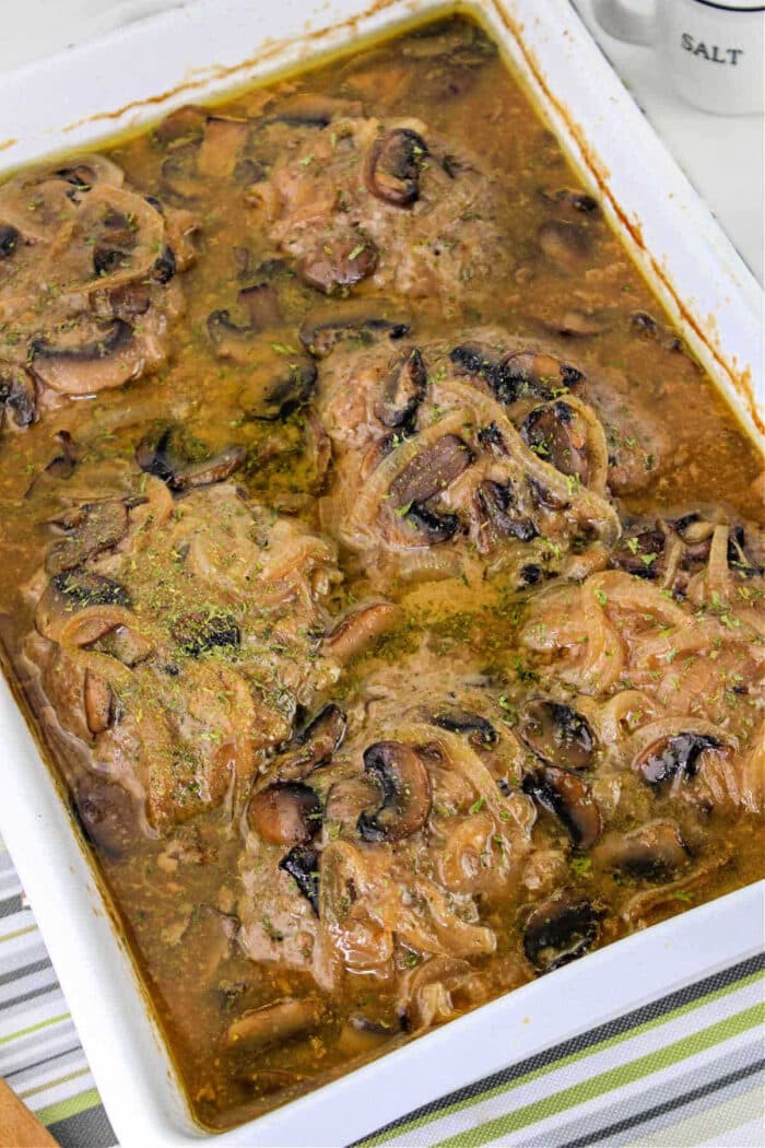 Baked pork chops in savory gravy with mushrooms and onions, reminiscent of classic Hamburger Steak, served in a white casserole dish.