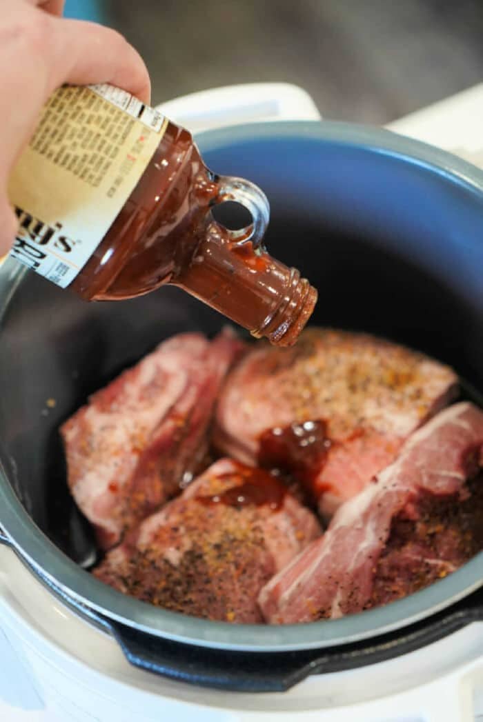Barbecue sauce being poured onto seasoned pork butt in an Instant Pot, ready for a flavorful slow-cooked meal.
